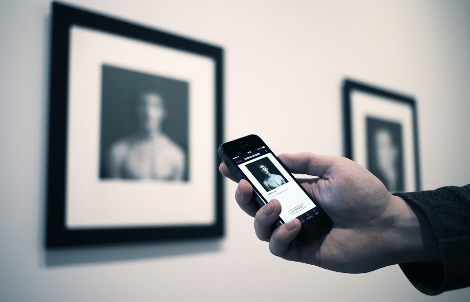 A hand holding a phone up to framed photographs in a gallery