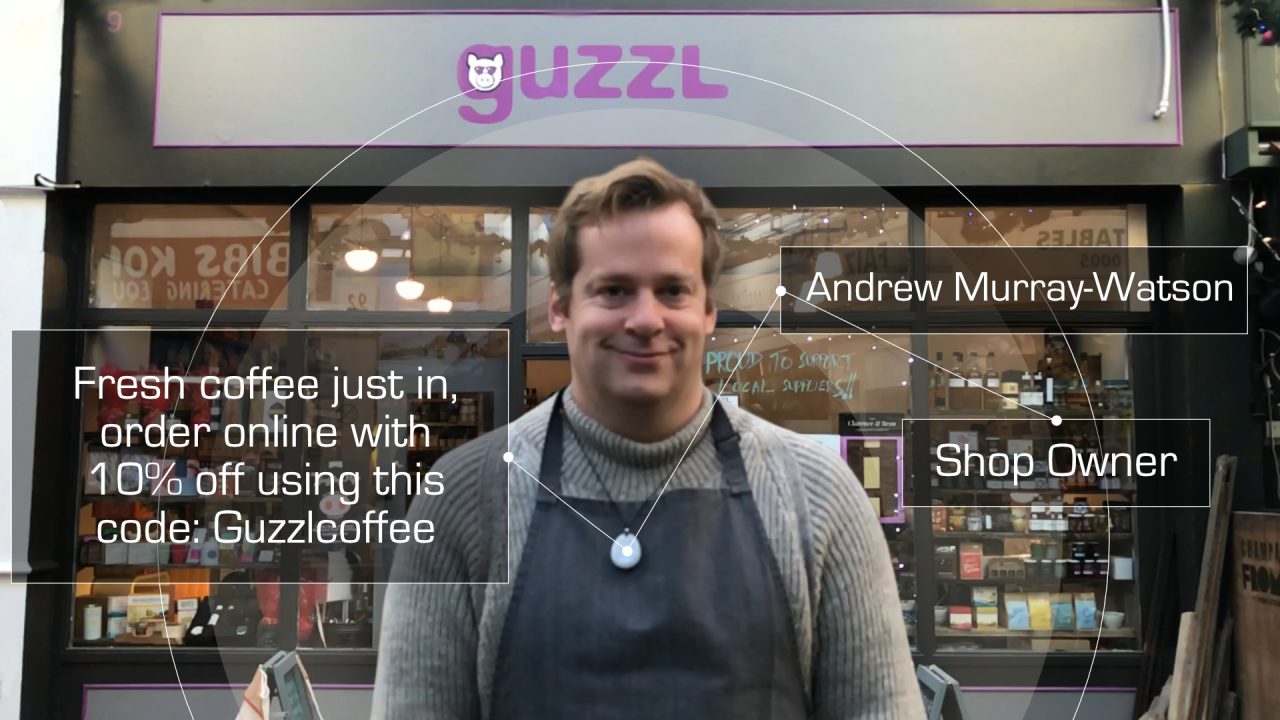 A shopkeeper in an apron outside the Guzzl shop wearing a Hex Beacon, with an overlaid post offering 10% off coffee
