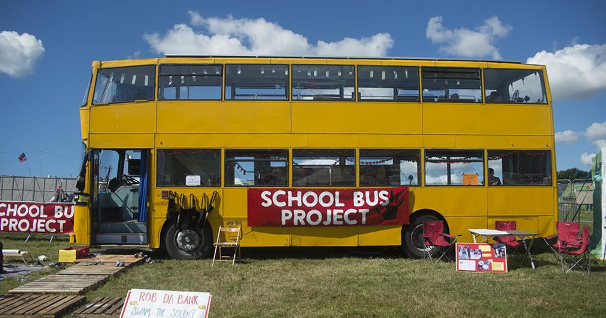 The School Bus Project's yellow double-decker bus parked on grass, with a pop-up classroom outside